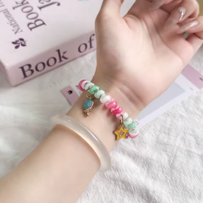Hand wearing a colorful beaded bracelet with star-shaped charms on a light background.